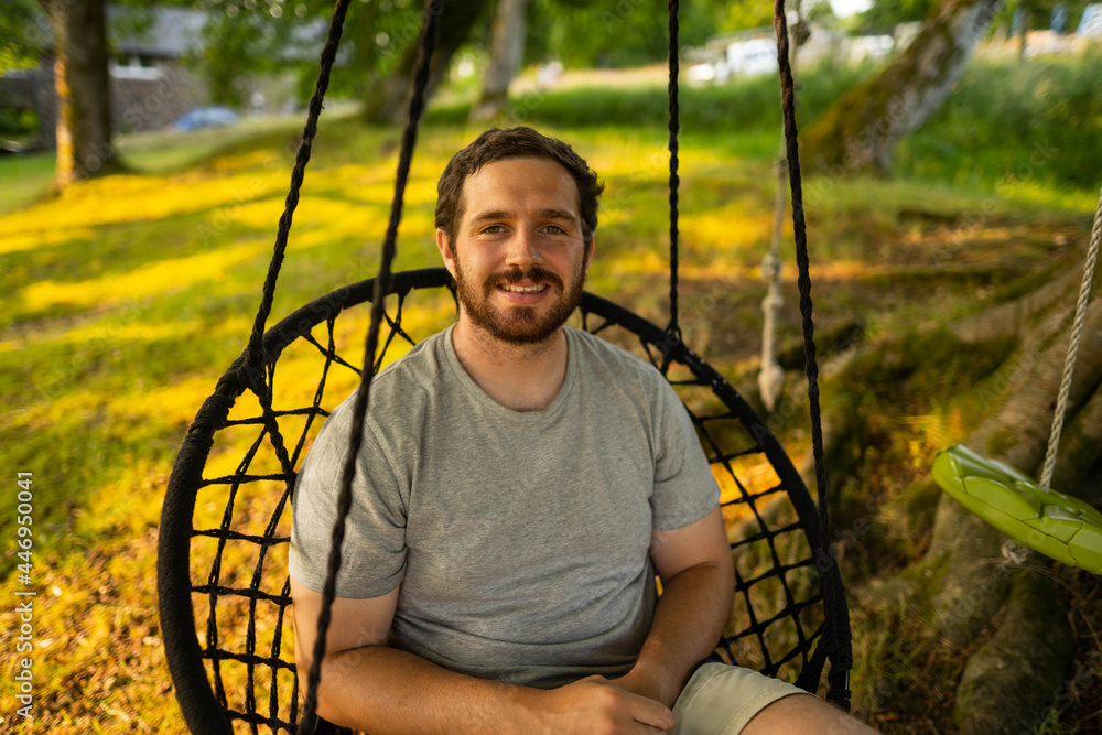 Photo of a attractive young guy relaxing on a hammock in the middle of nature. It is a summer day in the forest and he has a happy smile