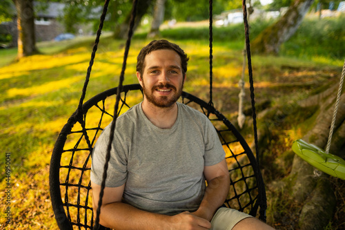Obraz na płótnie Photo of a attractive young guy relaxing on a hammock in the middle of nature. It is a summer day in the forest and he has a happy smile w salonie