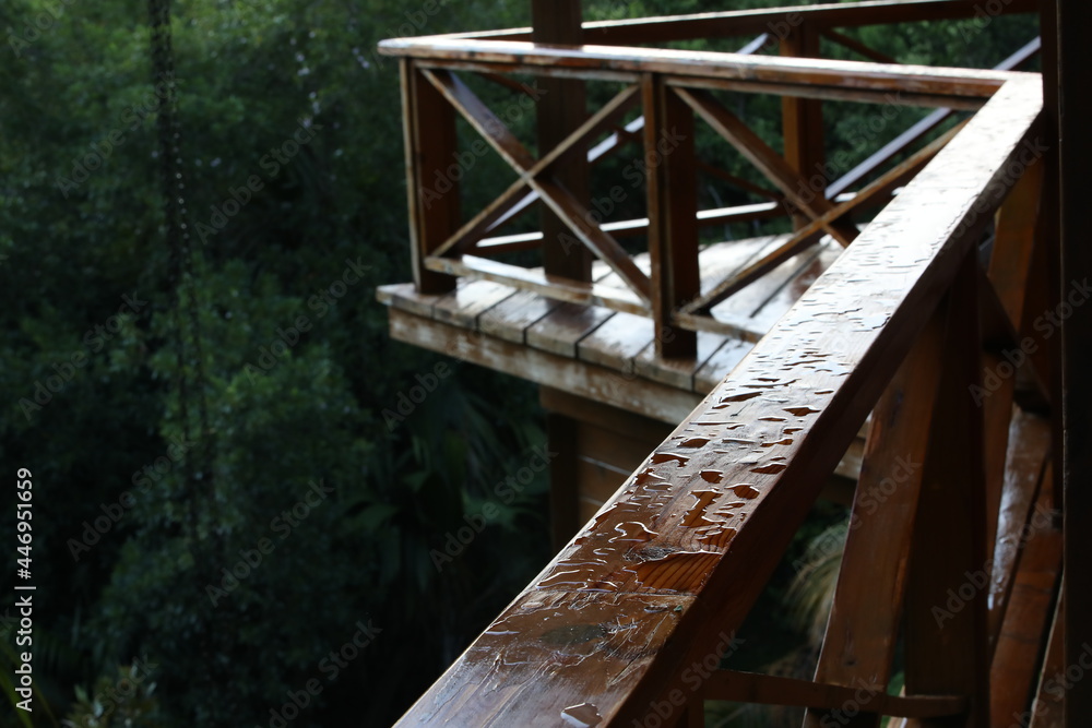 Raindrops on the wooden terrace.An upper balcony with wet railings on a green forest background.Close-up Raindrops on the wooden terrace.An upper balcony with wet railings on a green forest background.Close-up