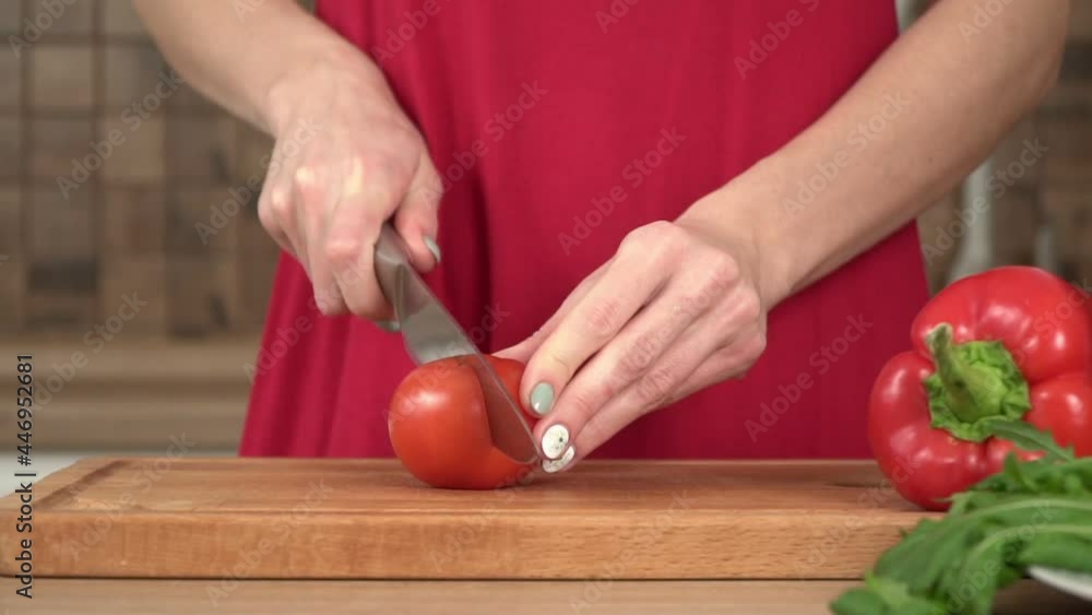 A woman in the kitchen cuts a red tomato with a knife, slow motion A woman in the kitchen cuts a red tomato with a knife, slow motion