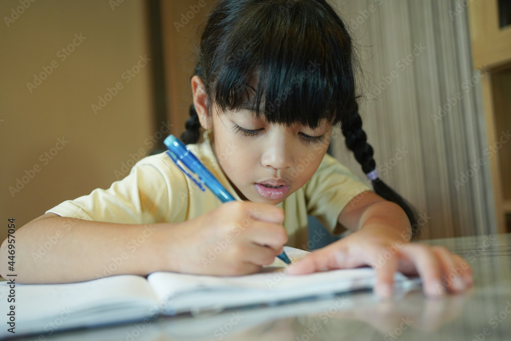 Asian student child girl writing on the paper book. Asian genius student doing a homework at home. education , study and learning concept. Asian student child girl writing on the paper book. Asian genius student doing a homework at home. education , study and learning concept.