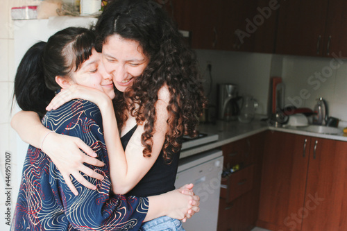 happy portrait of two women / lesbian couple in love cuddling hugging each other at home kitchen