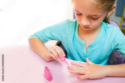 The girl in a turquoise T-shirt paints her nails with pink nail polish.