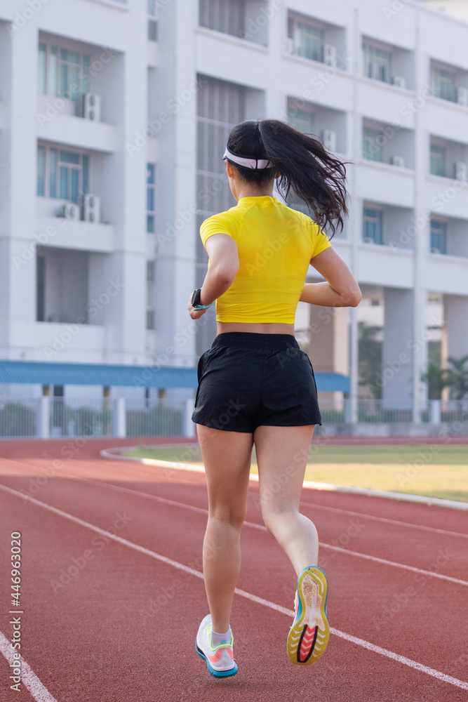 A young Asian woman athlete runner jogging on running track in city stadium in the sunny morning to keep fitness and healthy lifestyle. Young fitness woman runs on stadium track. Sport and recreation A young Asian woman athlete runner jogging on running track in city stadium in the sunny morning to keep fitness and healthy lifestyle. Young fitness woman runs on stadium track. Sport and recreation
