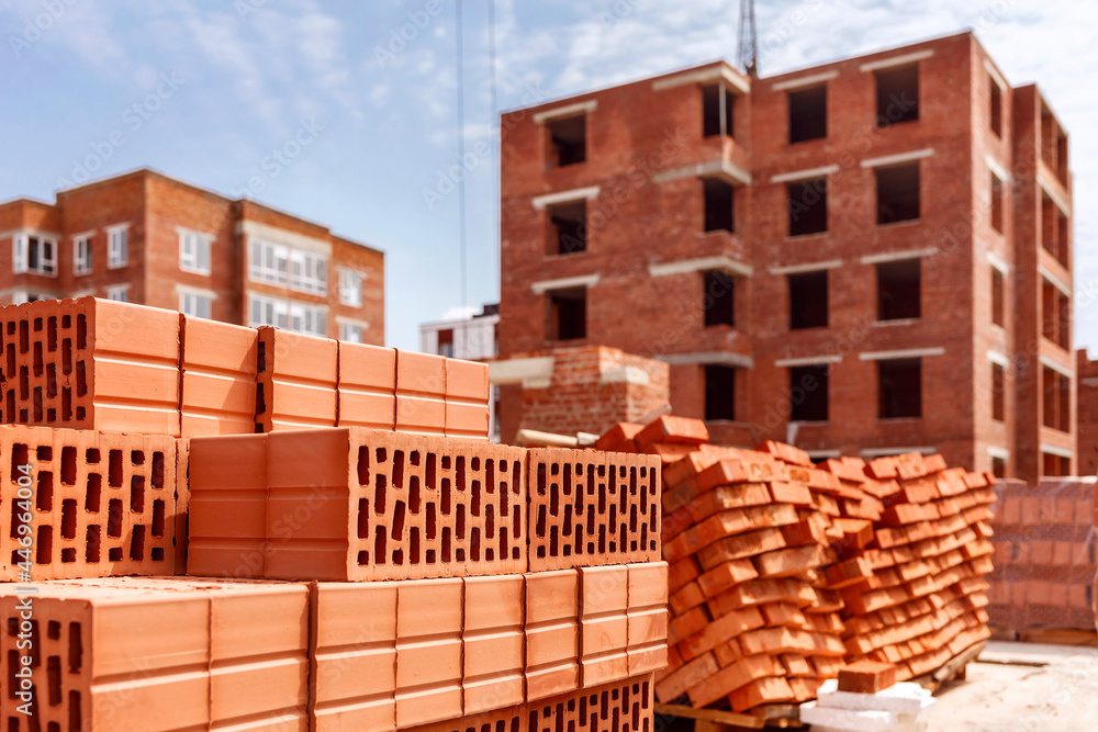 Pallets with bricks on the background of a multi-storey building. Construction site with brick pellets Pallets with bricks on the background of a multi-storey building. Construction site with brick pellets