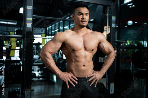 Handsome shirtless adult Asian men sweating while lift up the barbell workout machine for muscle part inside of fitness gym. Bodybuilding athlete sport training for body strength and good health.