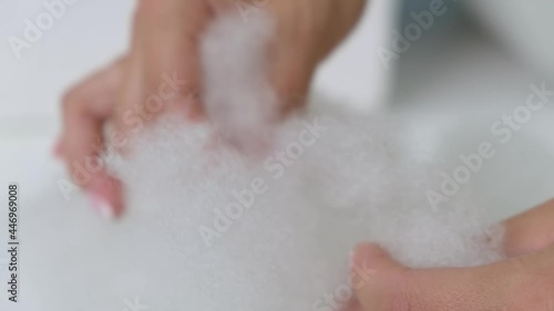 Close-up. The girl touches the white voluminous artificial fluff and sometimes breaks it