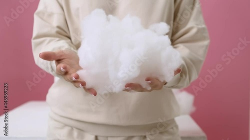 Medium shot. A girl in a vanilla-colored hoodie on a pink background and squeezes a voluminous artificial filler of white color