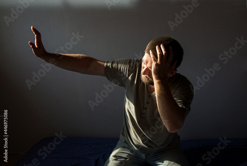 a young man with a beard hides his hand from the light, holding his head with the other hand. The concept of headache, hangover, photophobia. Close-up portrait photo