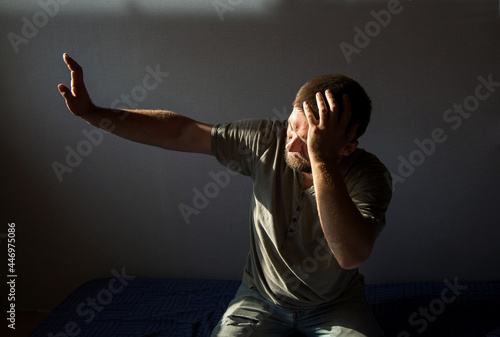 Foto a young man with a beard hides his hand from the light, holding his head with the other hand