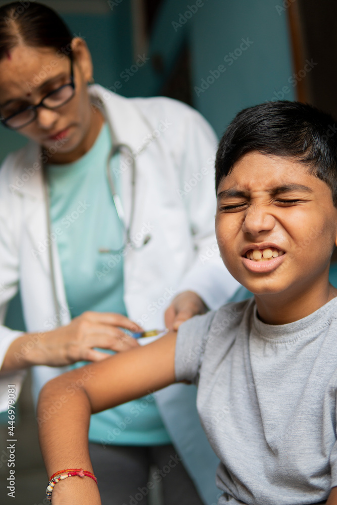 Obraz premium Young Indian boy receiving an injection by female doctors and shouting. 