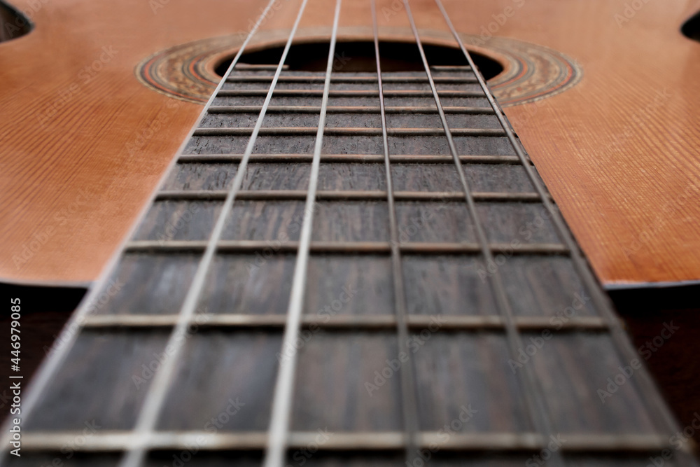 Close-up of old acoustic guitar fretboard with selective focus in the center. Neck perspective with blurred soundhole and strings. Music concept Close-up of old acoustic guitar fretboard with selective focus in the center. Neck perspective with blurred soundhole and strings. Music concept