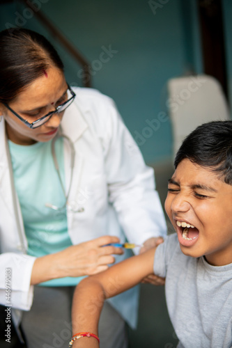 Young Indian boy receiving an injection by female doctors and shouting. 