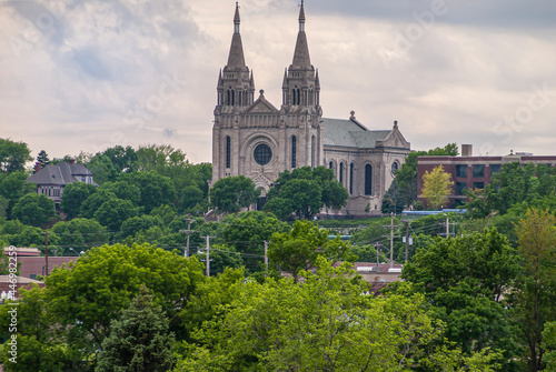 Sioux Falls, SD, USA - June 2, 2008: Beige stone Cathedral of Saint Joseph with 2 towers under white cloudscape and lots of green foliage up front. 