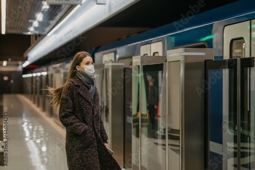 A woman in a medical face mask is waiting for an arriving train on the subway.