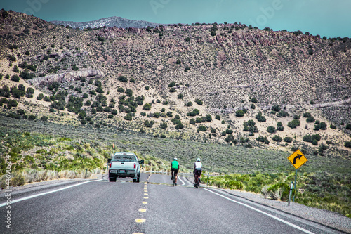 Bicyclers being passed by truck on two land Lonliest Highway in America through Nevada with scrub covered mountains in background.