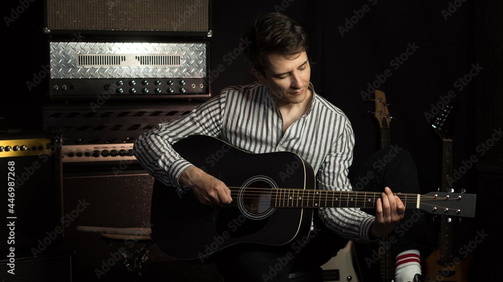 Obraz premium Handsome young acoustic guitar blues player performing his musical skills. Hipster Guitar player strumming. Handsome young male musician playing guitar in recording studio.