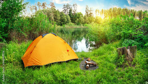 Orange tent on the river bank among green grass and trees