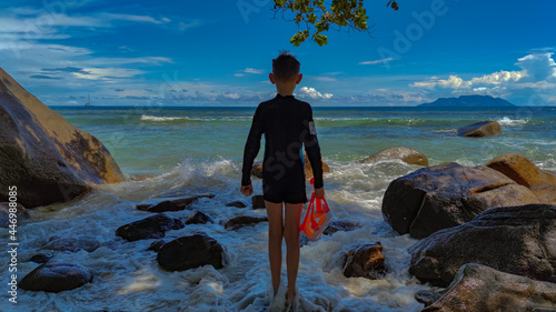 Back view on the boy standing on seashore in a swimsuit holding mask photo