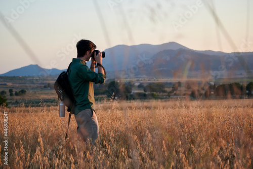 Man photographer with a backpack takes a photo in a meadow at sunset photo