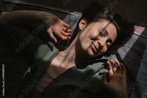 Woman laying in bed in sunny rays, stretching oneself and smiling.