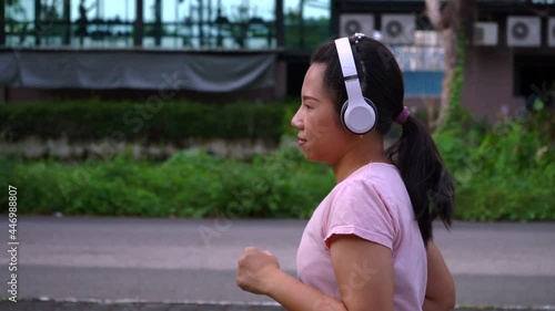 Young Asian woman with headphone jogging on the street in the morning. urban background. Runing exercise slow Motion photo