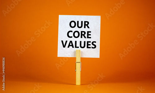 Our core values symbol. White paper with words 'Our core values', clip on wooden clothespin. Beautiful orange background. Business and our core values concept. Copy space.