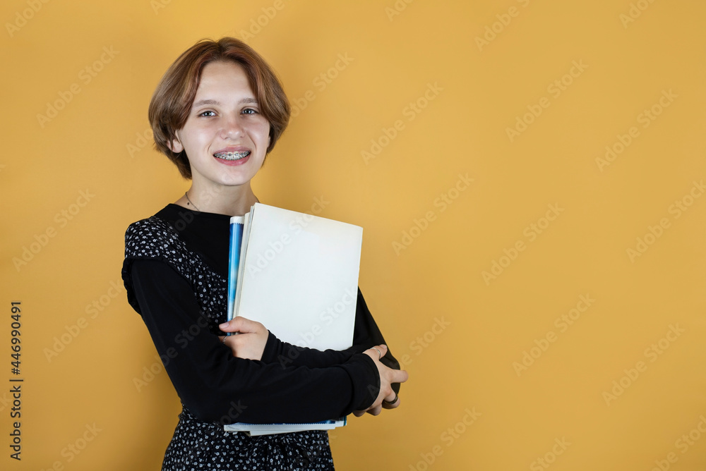 Teen girl with books and notebooks on a yellow background, place for text. The girl happily goes to high school. The concept of back to school Teen girl with books and notebooks on a yellow background, place for text. The girl happily goes to high school. The concept of back to school