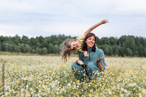 family photo. mom and daughter walk through a chamomile field in the summer. a woman and a child have fun and laugh