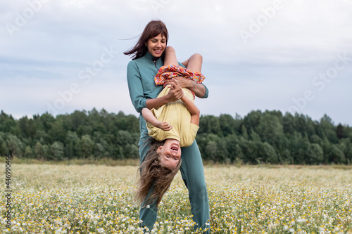 family photo. mom and daughter walk through a chamomile field in the summer. a woman and a child have fun and laugh