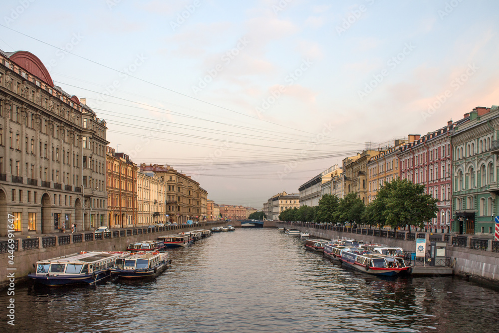 Moika River embankment with moored boats with reflections in the water and historical buildings in the early summer morning in Saint-Petersburg