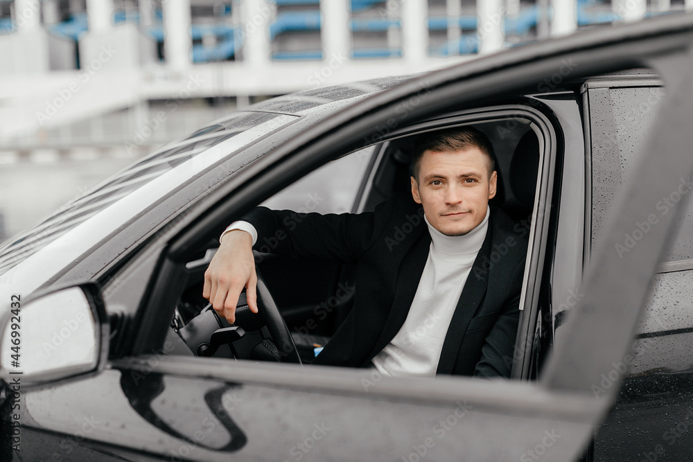 a handsome young man in a black suit is sitting in a car