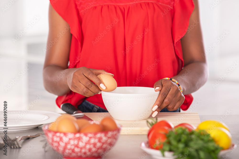 Close up of afro american woman holding an egg to the edge of a bowl Close up of afro american woman holding an egg to the edge of a bowl