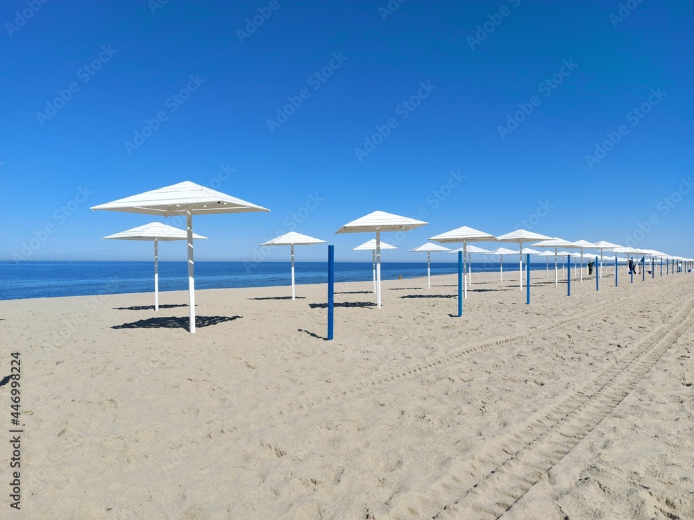Daytime view of an empty sandy beach with white umbrellas
