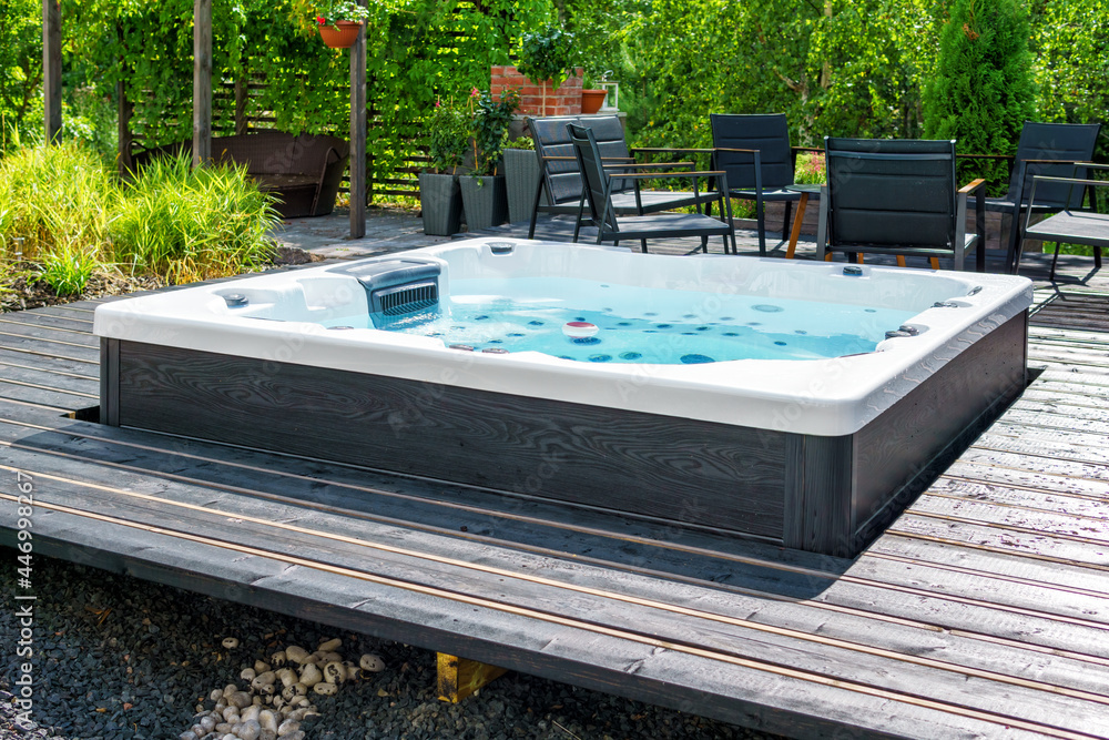 Obraz Large hot tub embedded in the backyard terrace. A sunny summer's day in the shelter of a green garden. Everyday luxury and relaxation in your own backyard. Spa complex, vacation and traveling concept.