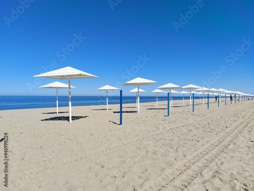 Daytime view of an empty sandy beach with white umbrellas © black_mts