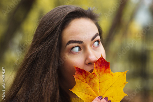 Young woman with autumn leaves in hand and fall yellow maple garden background