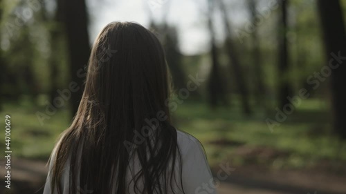 Slow motion shot of young woman walk and turn around in a park on a sunny summer day