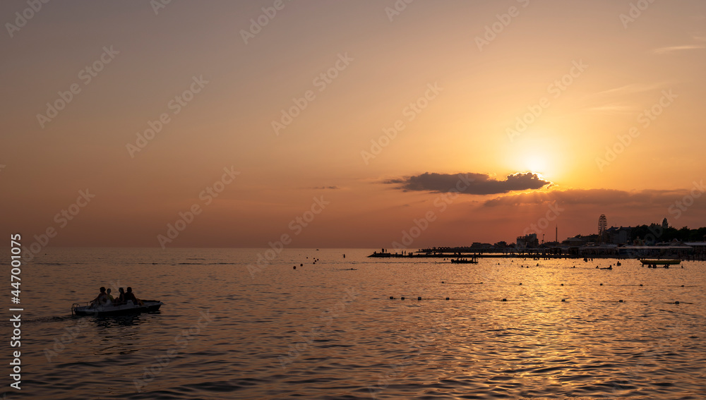 Red sunset over the dark evening sea, where there are many people swimming. Summer landscape