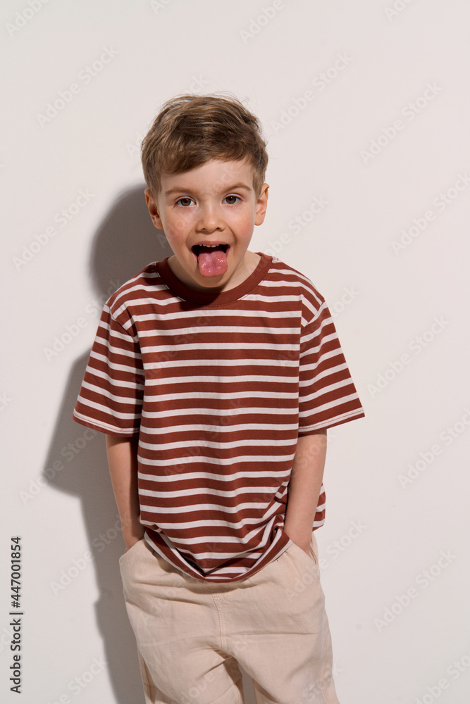 a boy in a T-shirt shows his tongue against a white wall a boy in a T-shirt shows his tongue against a white wall