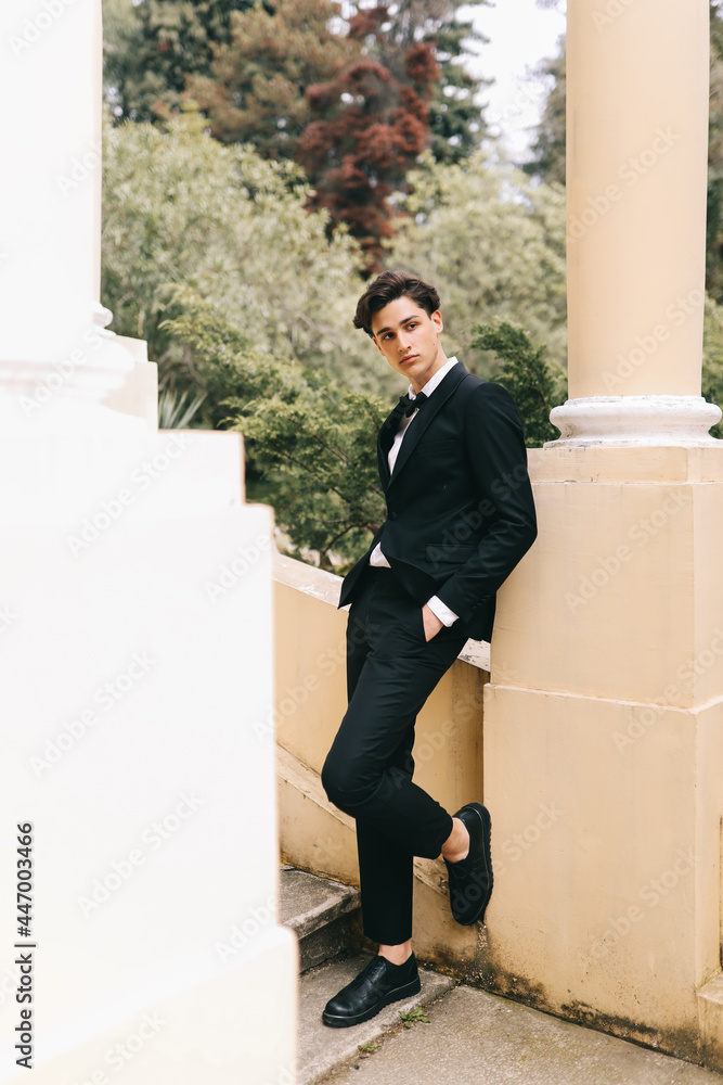 A beautiful fashionable stylish cool young man in an elegant wedding suit poses and walks alone among plants and palm trees in an old park in nature outdoors, selective focus A beautiful fashionable stylish cool young man in an elegant wedding suit poses and walks alone among plants and palm trees in an old park in nature outdoors, selective focus