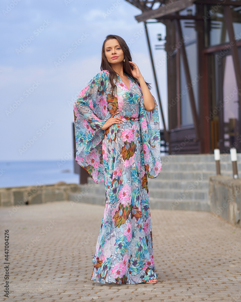 Full length outdoor portrait of young elegant tall woman in colorful blue dress with floral print walking at sea ambankment on a sunny day Full length outdoor portrait of young elegant tall woman in colorful blue dress with floral print walking at sea ambankment on a sunny day