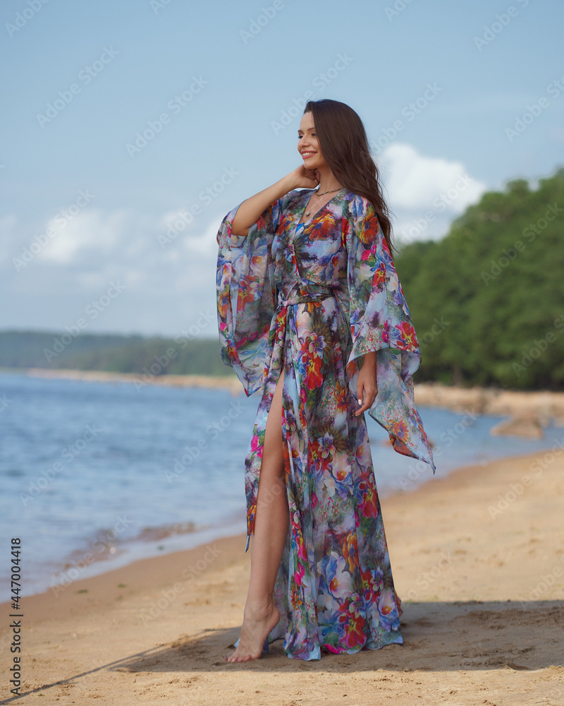 Elegant woman in colorful tunic standing and posing at sandy beach on s ummer sunny day.