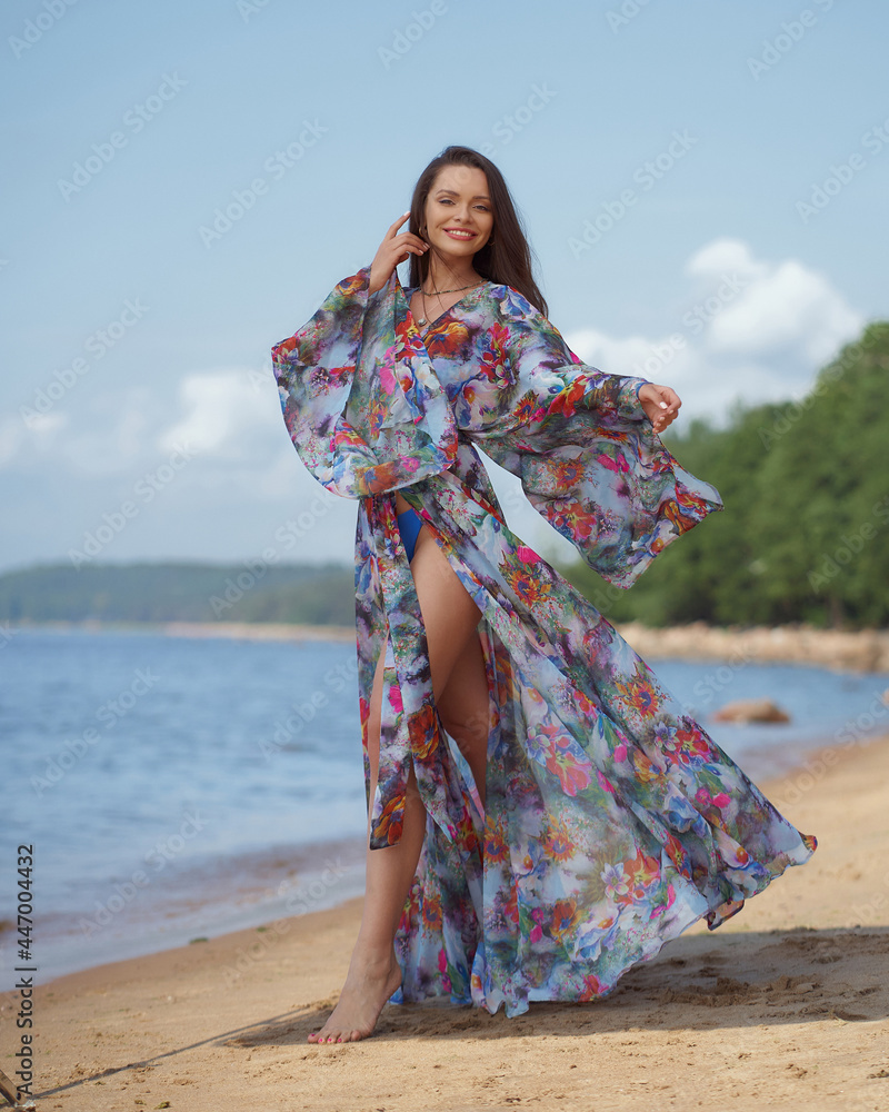 Elegant woman in colorful tunic standing and posing at sandy beach on s ummer sunny day.