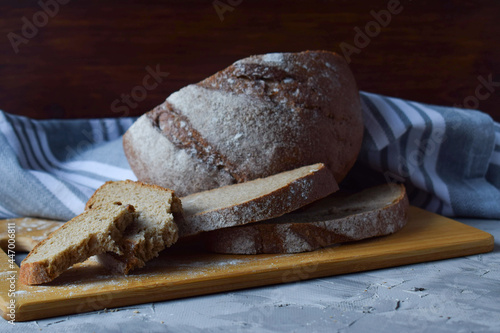 slices of sliced freshly baked rye bread on a wooden board, a cotton napkin, a place for text. Gray background, close-up.