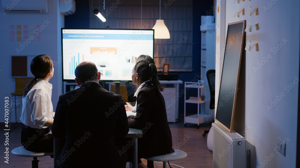 Multi ethnic diverse businesspeople working in business company meeting office room brainstorming marketing strategy late at night. Entrepreneur woman presenting financial graphs on monitor Multi ethnic diverse businesspeople working in business company meeting office room brainstorming marketing strategy late at night. Entrepreneur woman presenting financial graphs on monitor