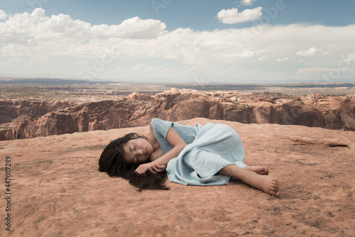 Asian girl in blue dress laying down and dreaming on edge of crater on red soail in Canyonlands National Park, USA photo