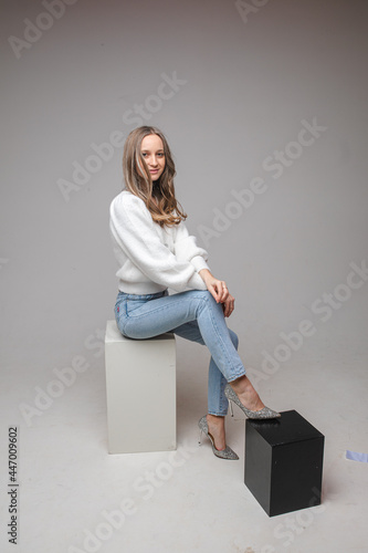 Attractive blonde woman in sweater and jeans in studio.