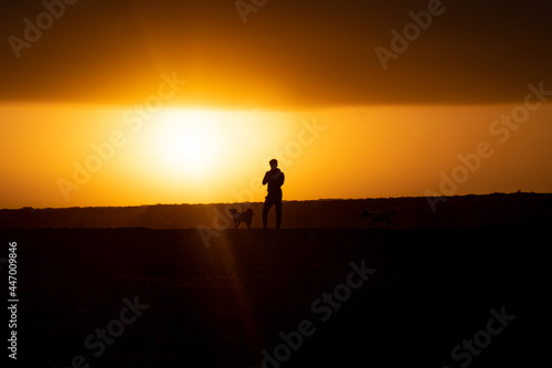 Young Man next to a Dog are Looking the Sunrise in the Desert at Punta Gallinas, with a Yellow Sky Full of Clouds in La Guajira, Colombia © Alexandre
