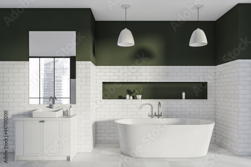 Bathtub and vanity in the industrial white bathroom with dark green details